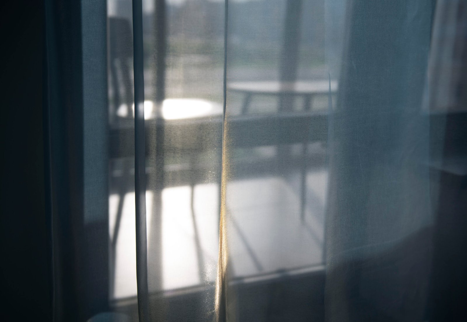 Blue sheer curtains with soft sunlight filtering through, creating blurred shapes behind them.