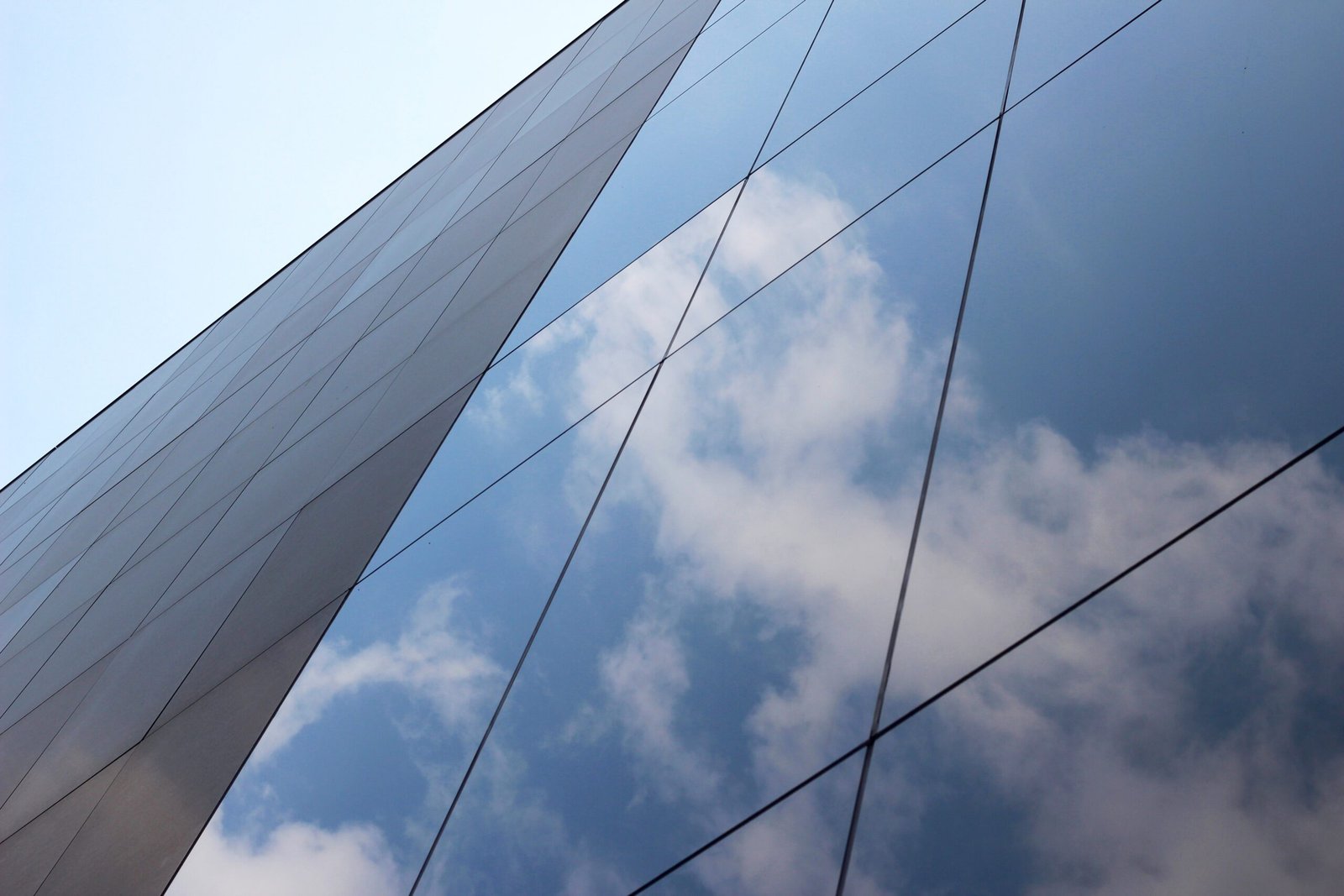 Diagonal white glass panels of a modern building with dark lines against a blue sky.