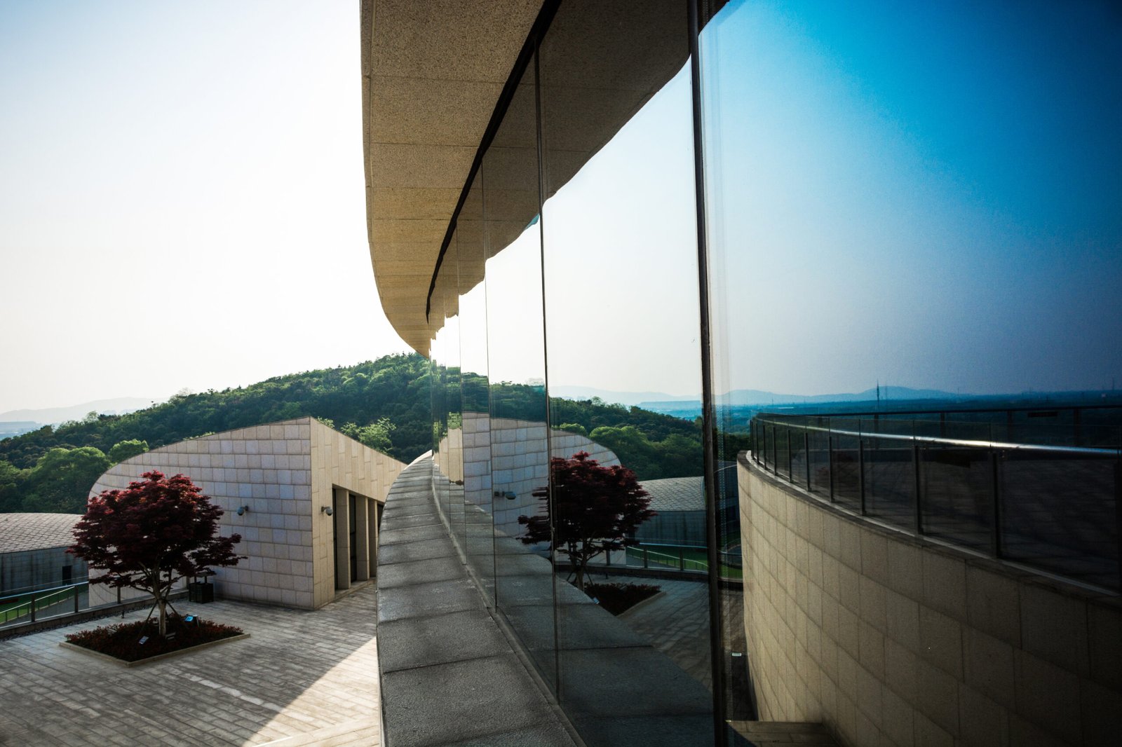 Modern beige building with a curved glass facade reflecting the sky and landscape.